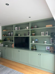 Custom sage green TV media wall with cabinets and open shelving